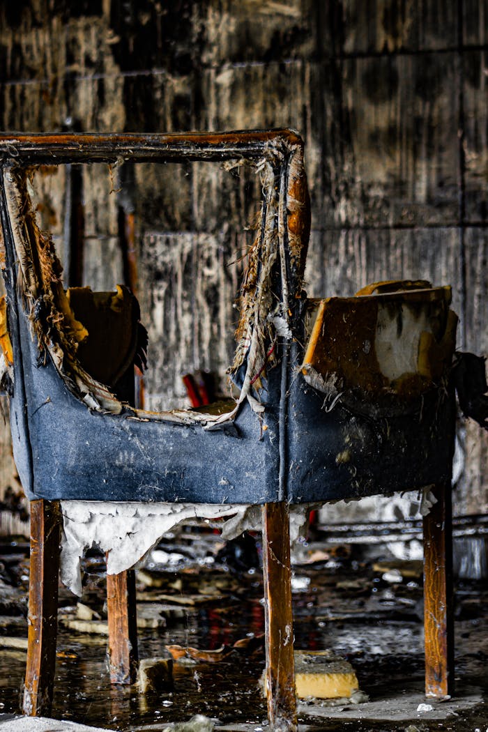 our-experience A worn, burnt chair in an old, abandoned room with peeling walls.